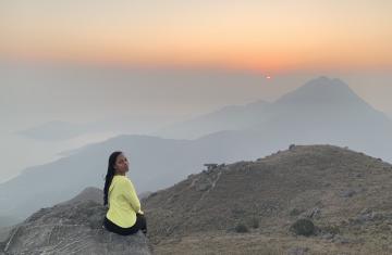 Taylor Doggett sits at a lookout point of Lantau Island's Sunset Peak trail, looking over her shoulder to smile at the camera