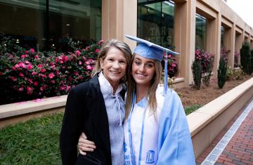 Karen Shelton and Erin Matson pose for a photo together outdoors, with Matson dressed in graduation regalia, following commencement.