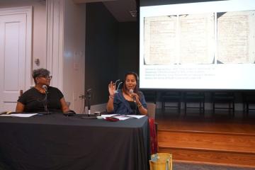 xRhiannon Giddens speaking on stage with Leoneda Inge, WUNC&rsquo;s race and Southern culture reporter, with a presentation on a screen behind them