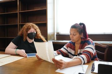 Rhiannon Giddens reading an archival paper in Wilson Library while seated next to her research assistant