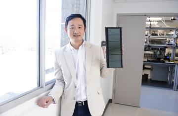 Jinsong Huang stands in a lab next to a window holding a solar panel 