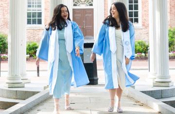 Twins Nathalie and Nicole walk and hold hands and look at each other with the Old Well in the background