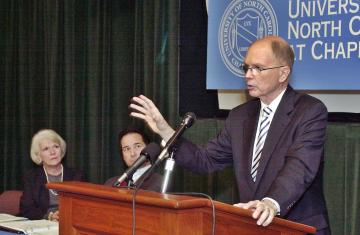 Chancellor Moeser stands behind a lecturn with his hand in the air at a press conference