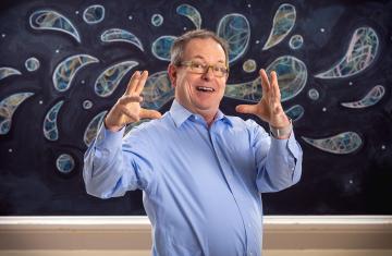 Keith Sawyer faces the camera with fun expression and hands in the air; a blackboard with water drop motif is in the background