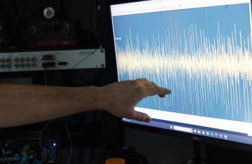A hand points out brain waves displayed on a computer monitor.