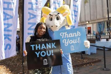 A Carolina student and mascot Rameses holding up signs thanking donors.