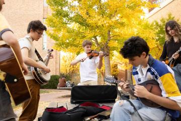 Carolina students playing fiddles and banjos in a circle on campus.