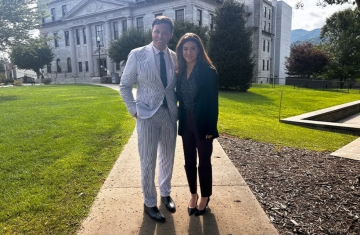 A man and a woman stand in business attire in front of a courthouse.