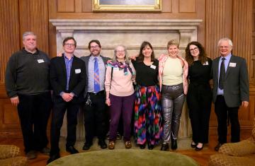 Eight Carolina Public Humanities staff pose for the camera in front of a fireplace.