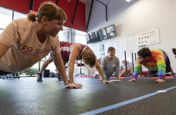 Four people do push-ups in a gym.