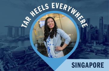 A woman stands in an office setting with a map pin graphic that surrounds her in blue that reads "Tar Heels Everywhere" and "Singapore."