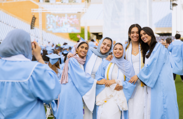 A group of five Carolina graduates smile for a phone camera.