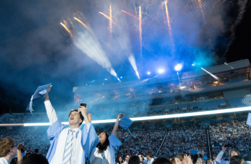 Two graduates holding their caps, looking excitedly at the fireworks at commencement.