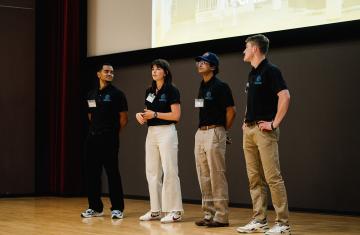 Four student coaches and peers stand on a stage.