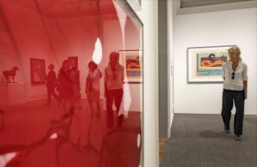An artwork featuring the color red in the foreground with a woman viewing other artworks in the "Color Triumphant" exhibit in the background