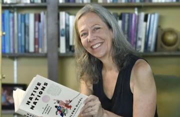 Portrait of Kathleen Duval reading book against library backdrop.