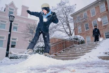 a student snowboards on icy snow in front of the South Building on Campus