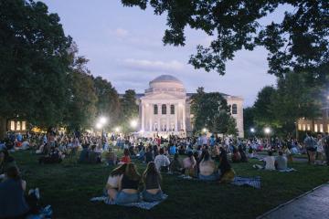 a wide angle photo of the backs of hundreds of students on Polk Place at twilight with a prominently lit Wilson Library facade in front of the crowd of students