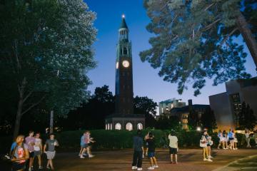 Students walk in foreground with dimly lit bell tower in background with deep blue sky