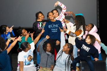 Jordyn Middleton poses at the center of a large group of children excitedly pointing at her in gratitude