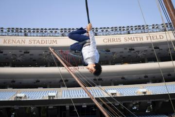Student does a flip assisted by bungee cables with Kenan Stadium seats and stadium lights in the background