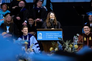 Mia Hamm smiles from the podium as she speaks with campus dignitaries pictured behind her seated on risers