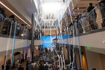 Streamers fall in atrium of new building with full crowd on ground level and in two levels of balconies