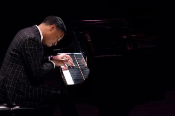 a zoomed in photo of a pianist in a suit performing in stark lighting