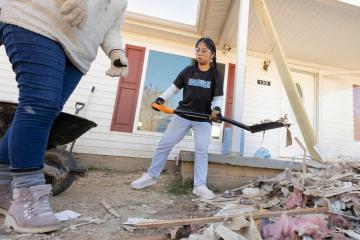 Student in Carolina Covenant shirt uses shovel to move debris in front of house