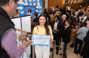 Person stands on staircase with a sign that reads "I matched in dermatology at U Chicago"