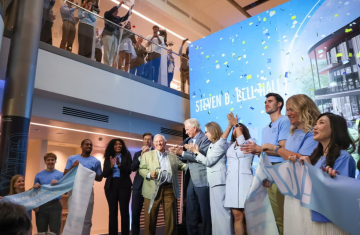 People at a ribbon cutting ceremony with a sign that reads "Steven D. Bell. Hall" in the background.