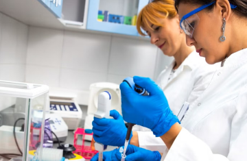 Two people work in a lab with lab coats and safety goggles on