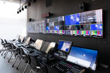 Production studio at the Curtis Media Center, with a wall of monitors above desks with audiovisual control panels in front of them