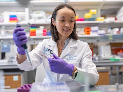 Scientist in white lab coat holds a pipette