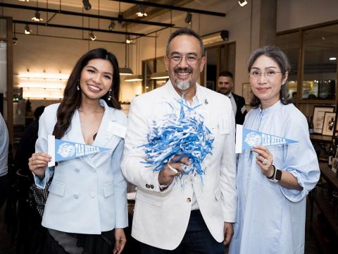 Three people holding up Tar Heel pennants and a pom-pom at an event