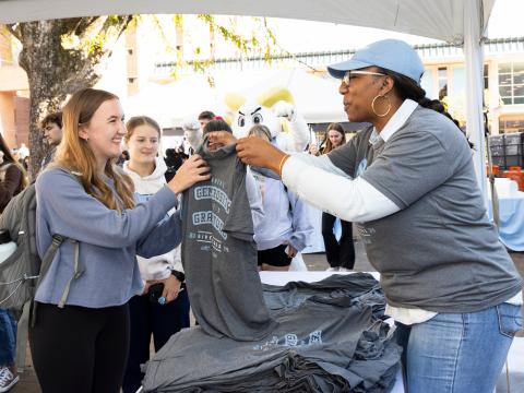 A student takes a tshirt from a faculty member at an on campus event