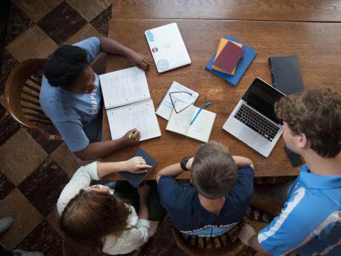 Carolina students interact at a desk with notebooks and laptops in front of them