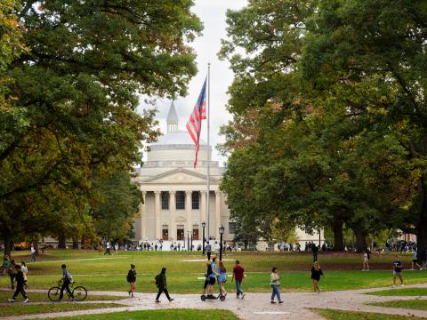 Students walking on Polk Place in front of Wilson Library with the American flag