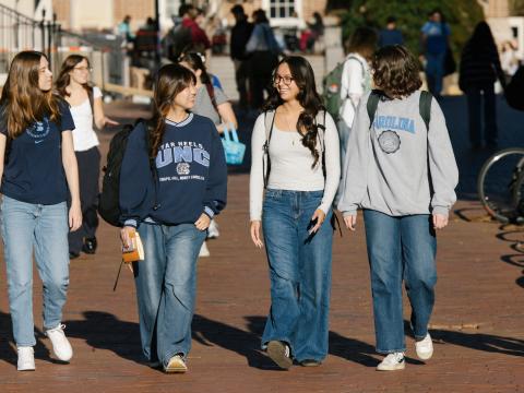 4 Carolina students walking along a sidewalk while talking to each other