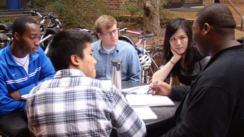 5 Carolina students sitting around a table, in conversation