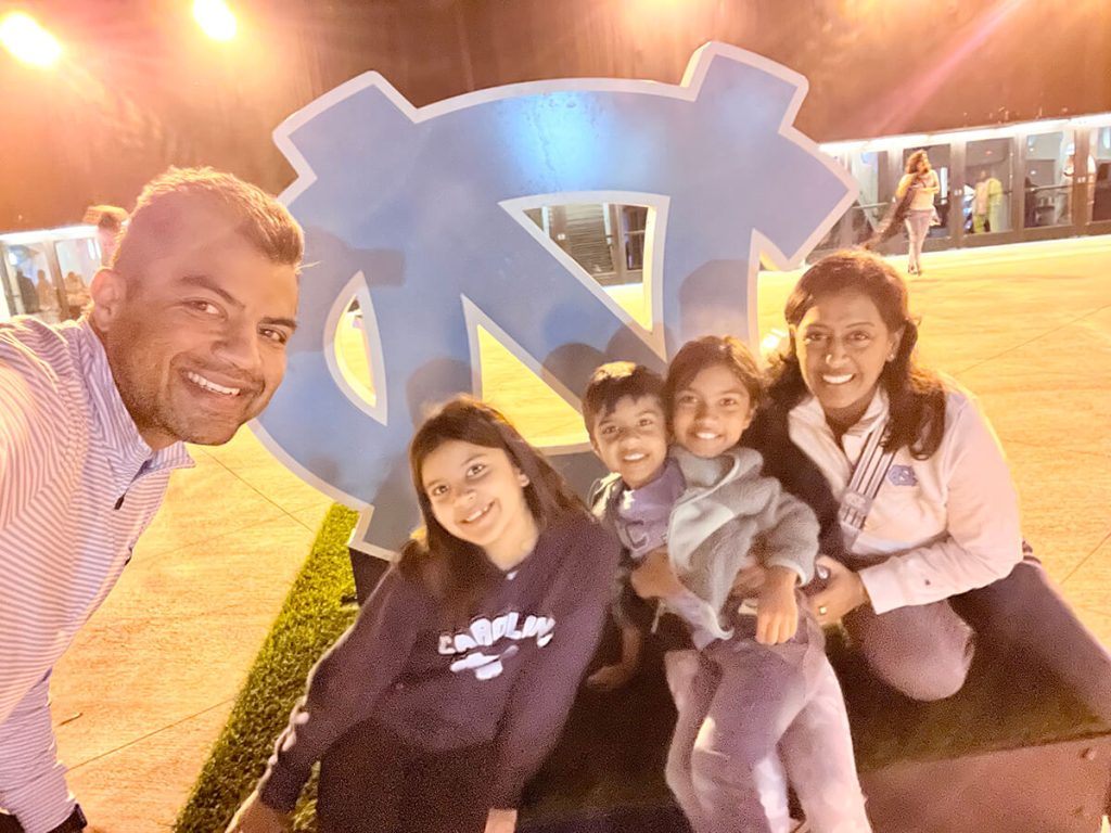 Nikin and Rashmi Shah with their three children in front of a UNC sign.